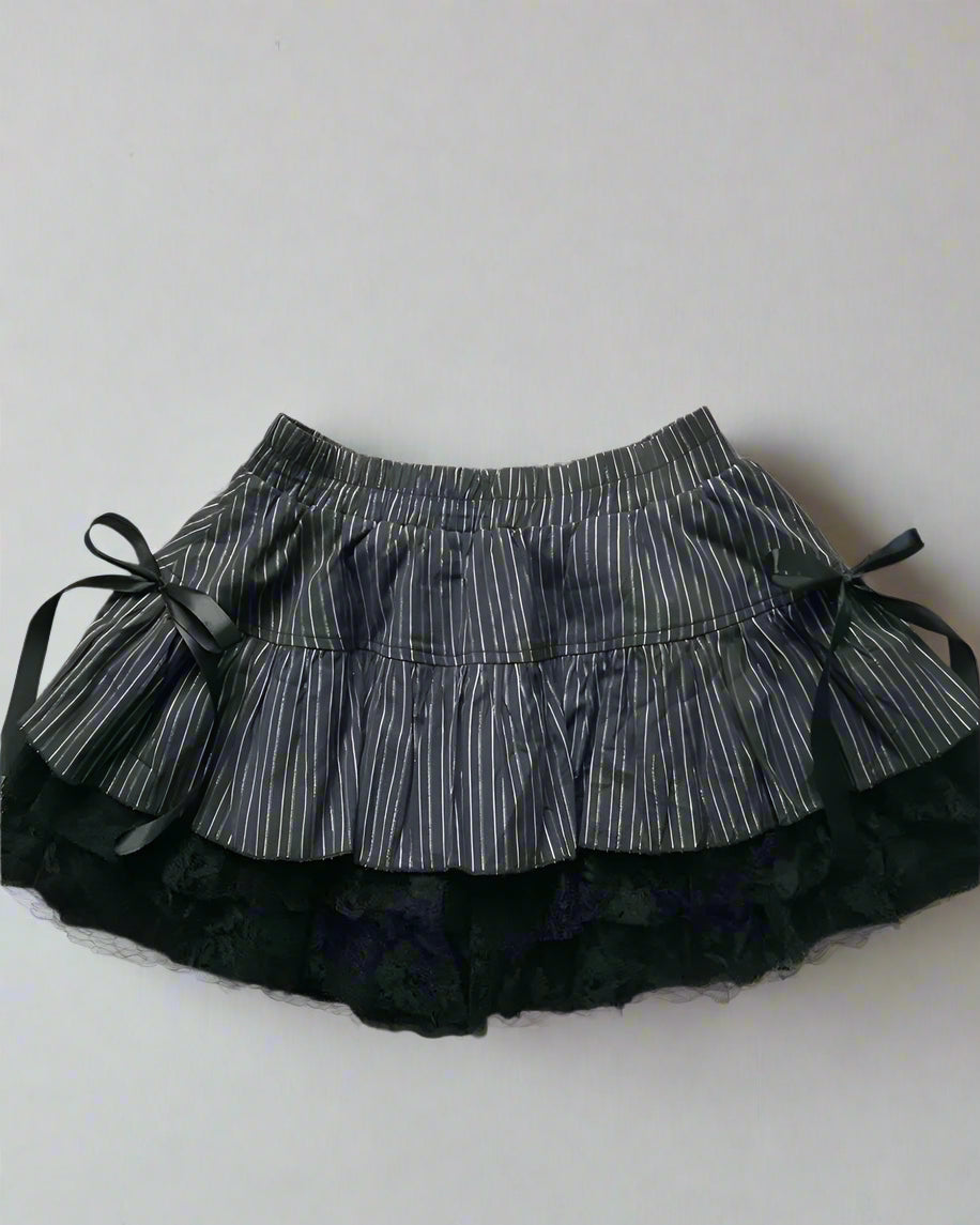 Black and white striped skirt with black shoes and hair ties on a light gray background