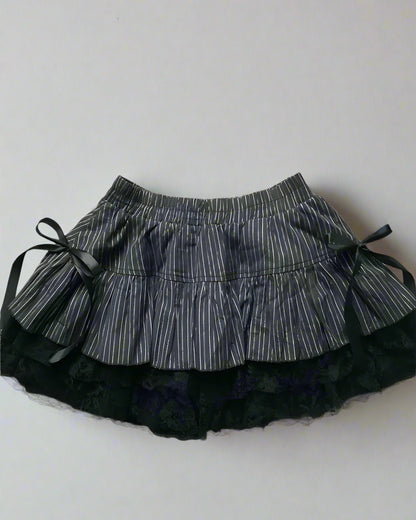 Black and white striped skirt with black shoes and hair ties on a light gray background